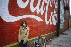 Dziewczyna stojąca pod murem z logo Coca-cola (foto: flickr)